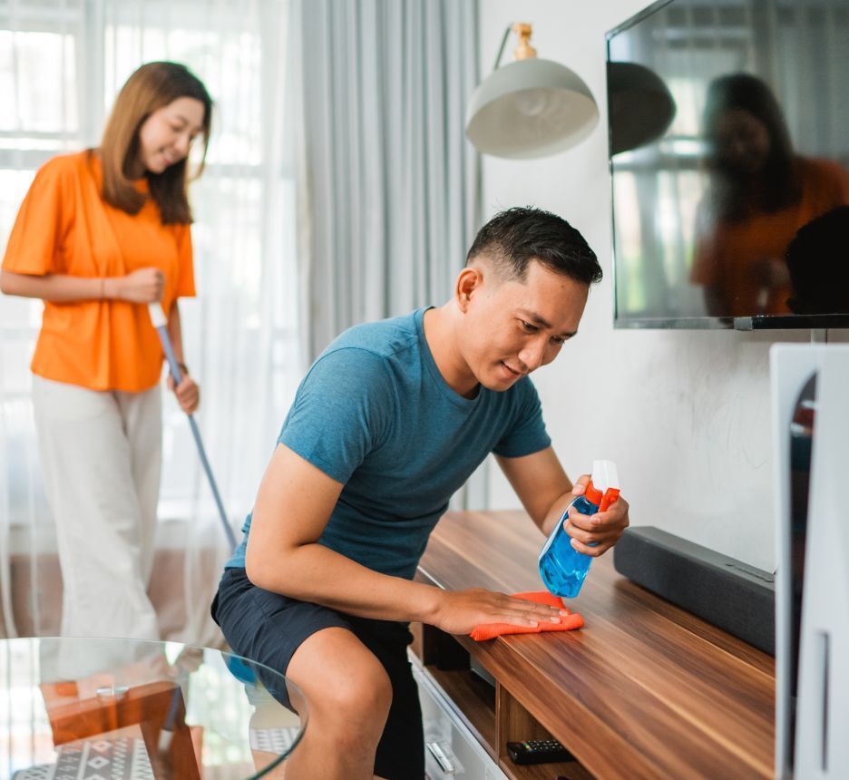 Man cleaning dust on a TV cabinet with his wife.