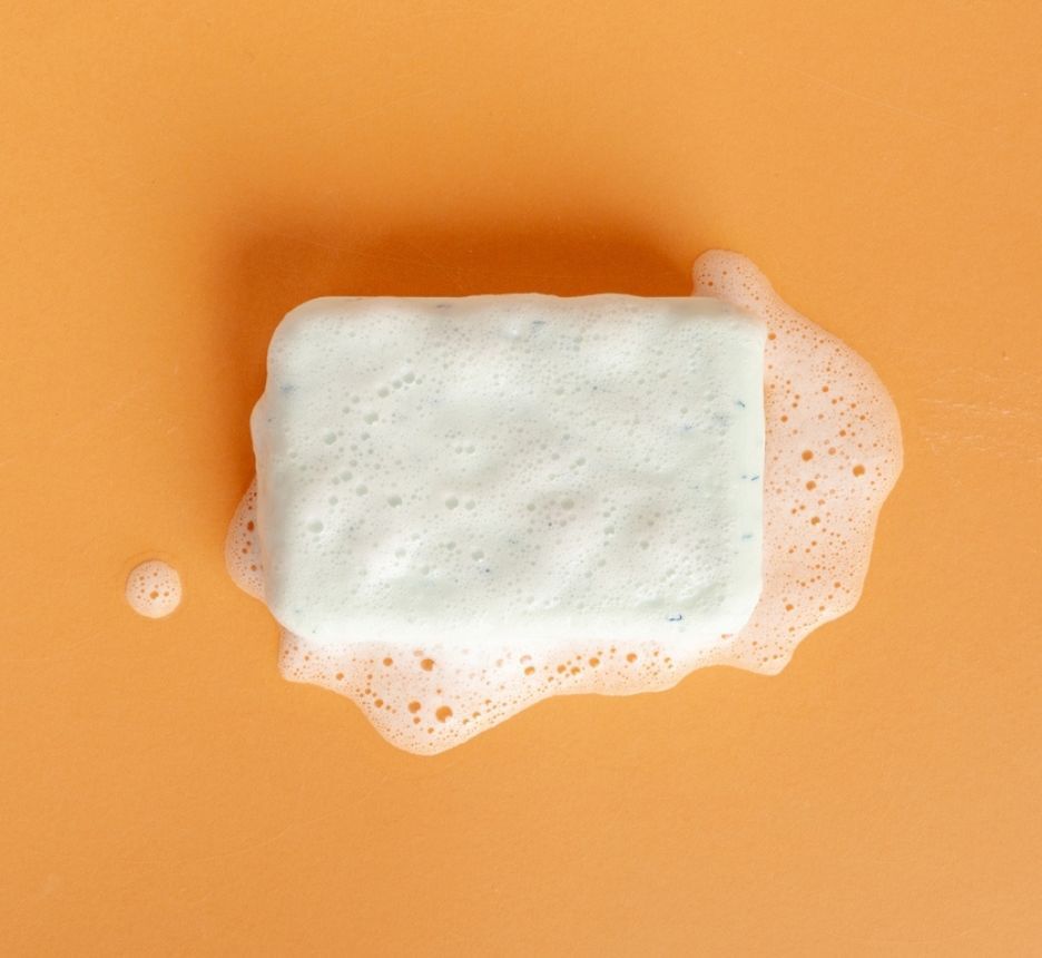 White soap bar with foam on orange background.