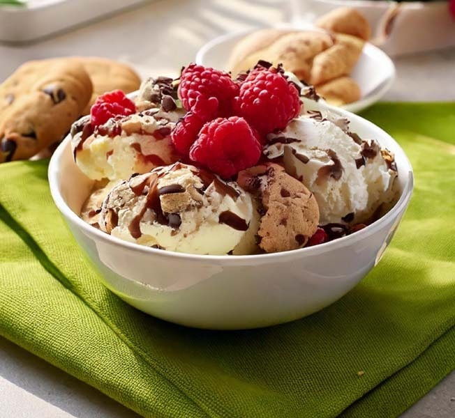 Scoops of non-dairy ice cream topped with raspberries in a bowl