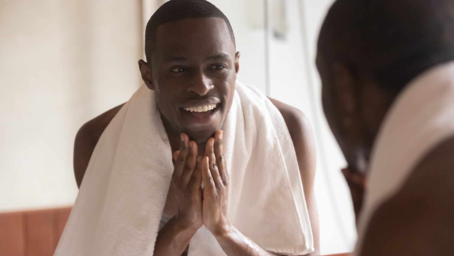 Young African American man looking at his face in the mirror after washing and shaving