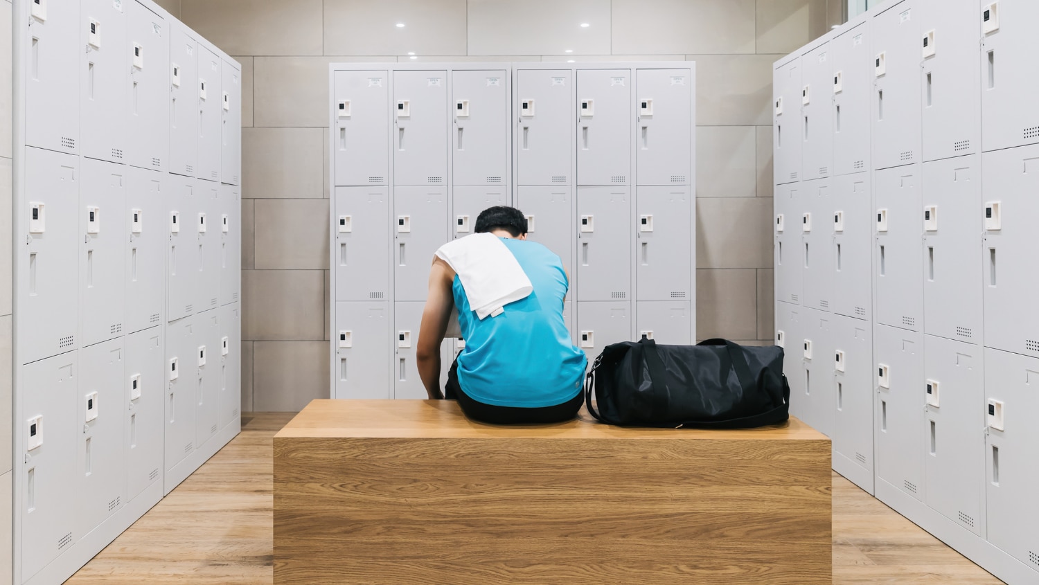 Back view of a male sitting in a gym locker room getting ready to take a shower