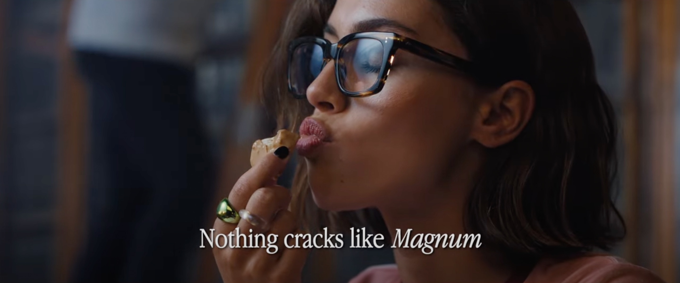 Women enjoying a Small cylinder-shaped bite-sized Magnum Bonbon Gold Caramel Billionaire ice cream, dipped in Magnum's signature cracking chocolate, laid out on an enticing background made of thick cracked golden caramel chocolate, oozing with vanilla ice cream and gooey sauce