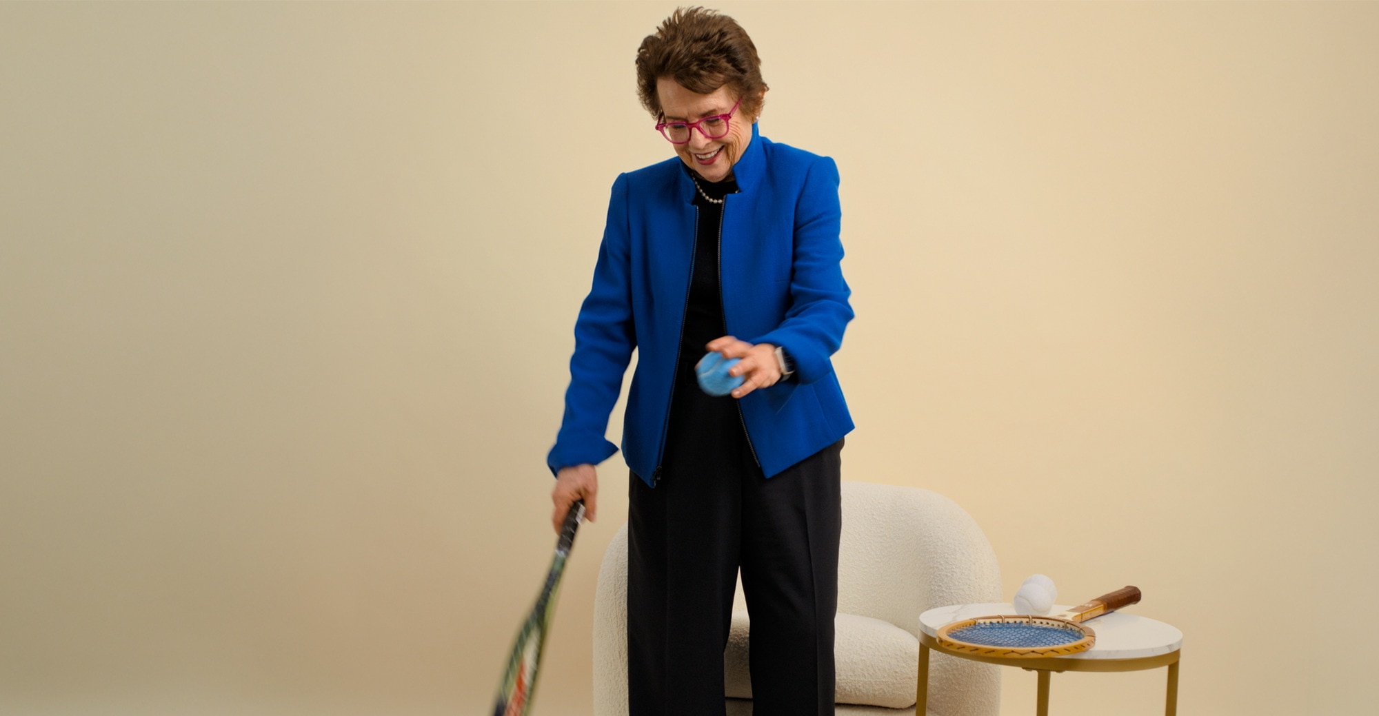Billie Jean King smiling with a tennis ball and racket in her hands