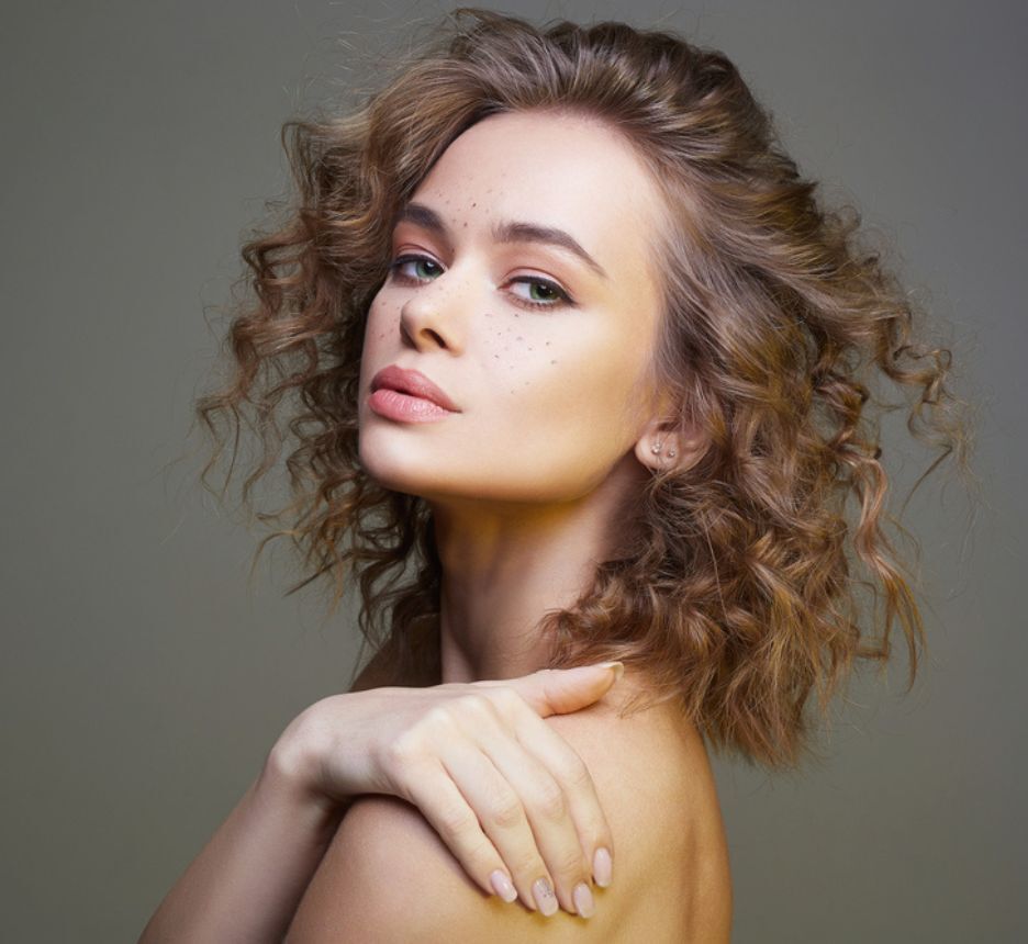 tóc xù tóc xù uốn lọn cô gái đặt tay lên vai và nhìn vào ống kính