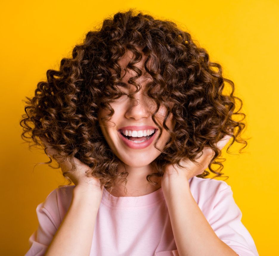 tóc xù tóc xù đũa cô gái cười tươi đang đưa hai bàn tay lên đỡ tóc