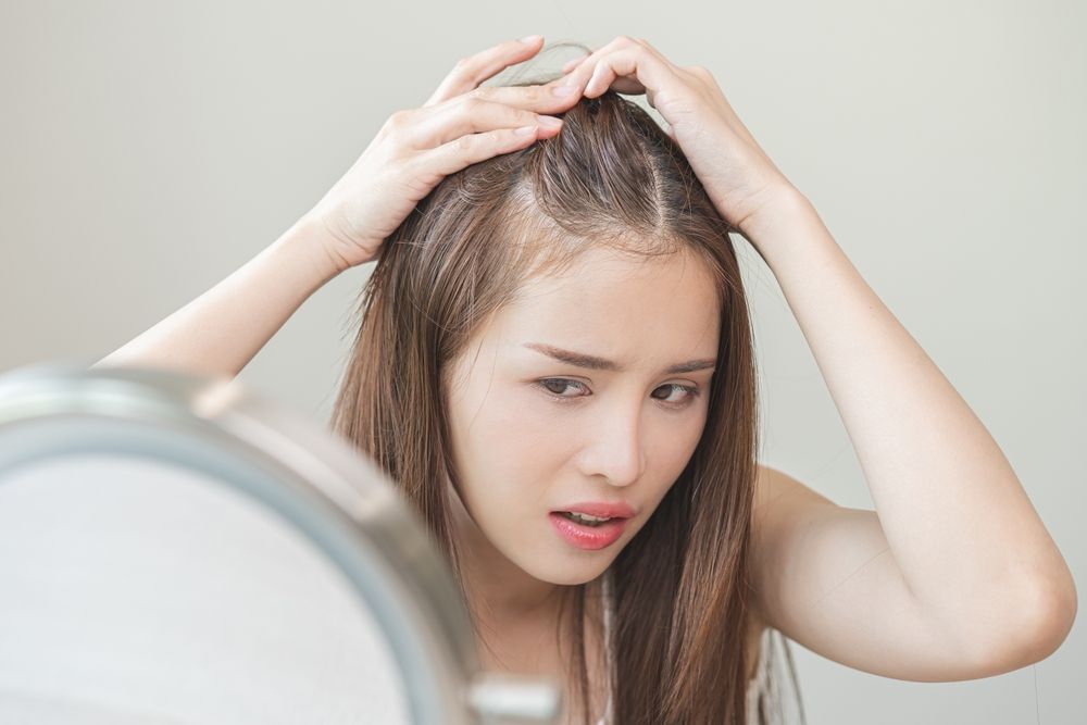 cấy tóc cô gái đang soi gương và quan sát chân tóc với vẻ mặt lo lắng
