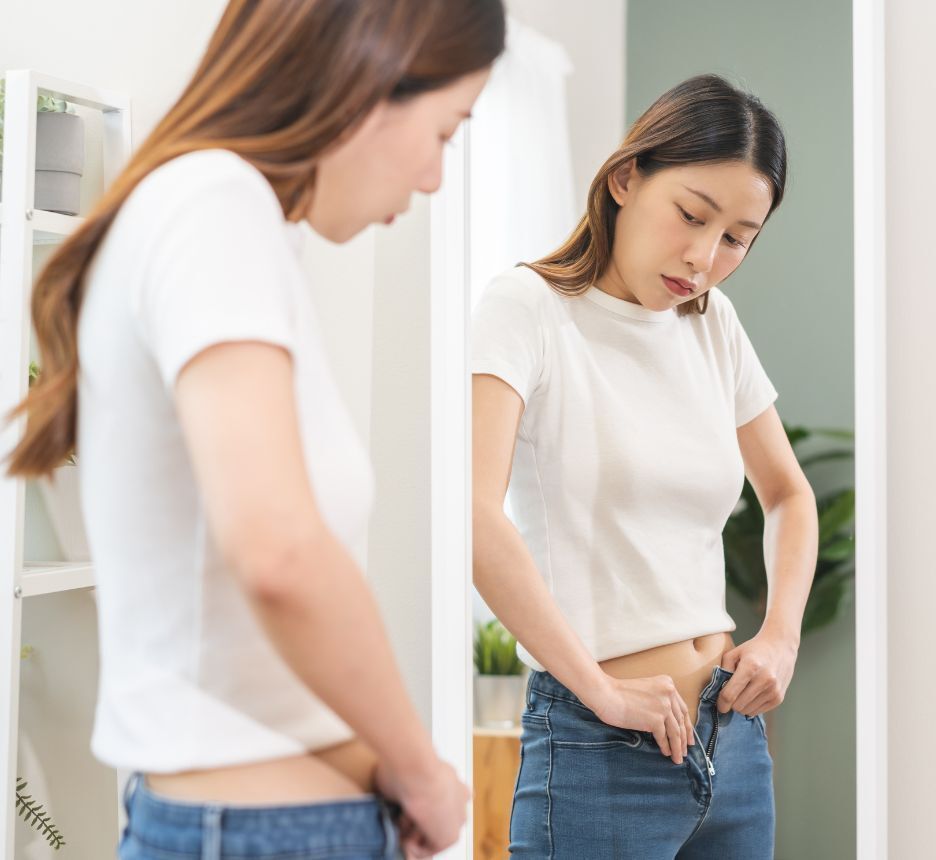 cách trị mụn ở mông nguyên nhân gây ra mụn nhọt ở mông cô gái đang soi gương và cô gắng kéo khóa chiếc quần chật