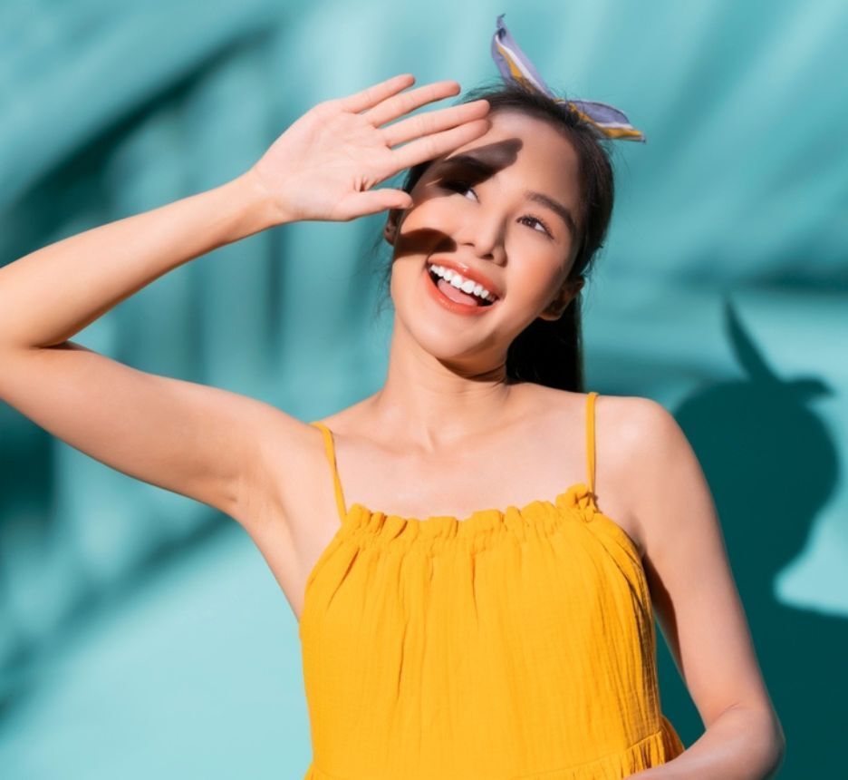 rụng tóc thiếu chất gì thường xuyên tắm nắng cô gái mặc váy hai dây màu vàng đang đưa tay che nắng