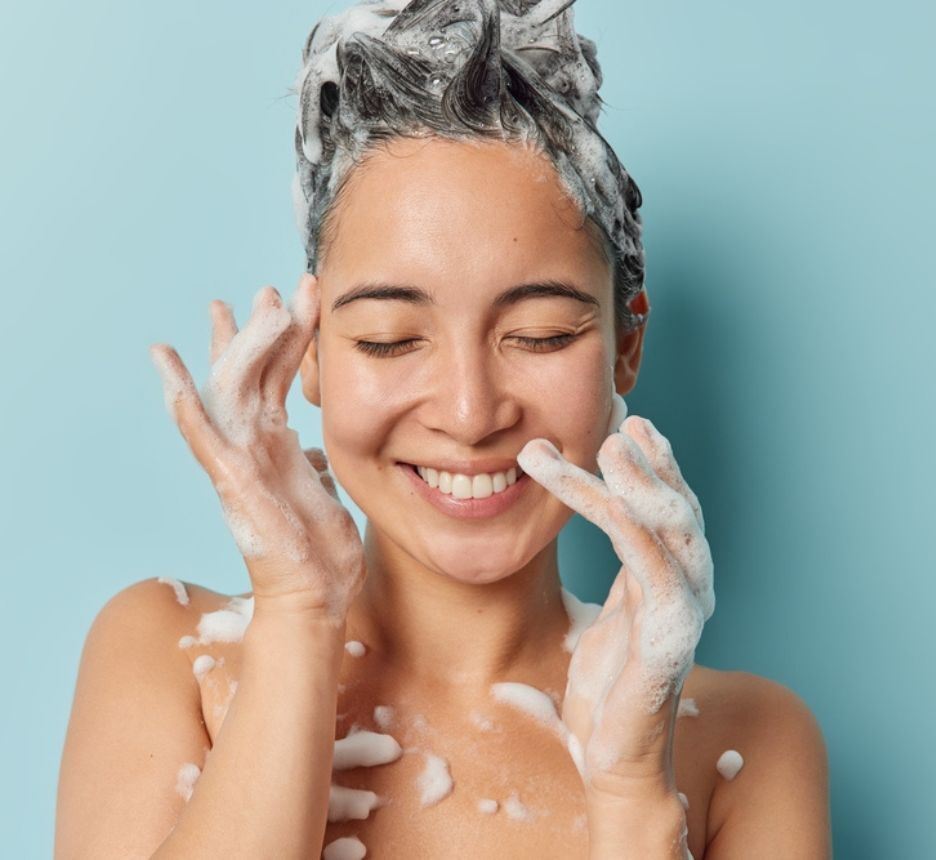 rụng tóc thiếu chất gì chọn sản phẩm chăm sóc tóc phù hợp cô gái đang nhắm mắt cười tươi với bọt xà phòng trên tóc