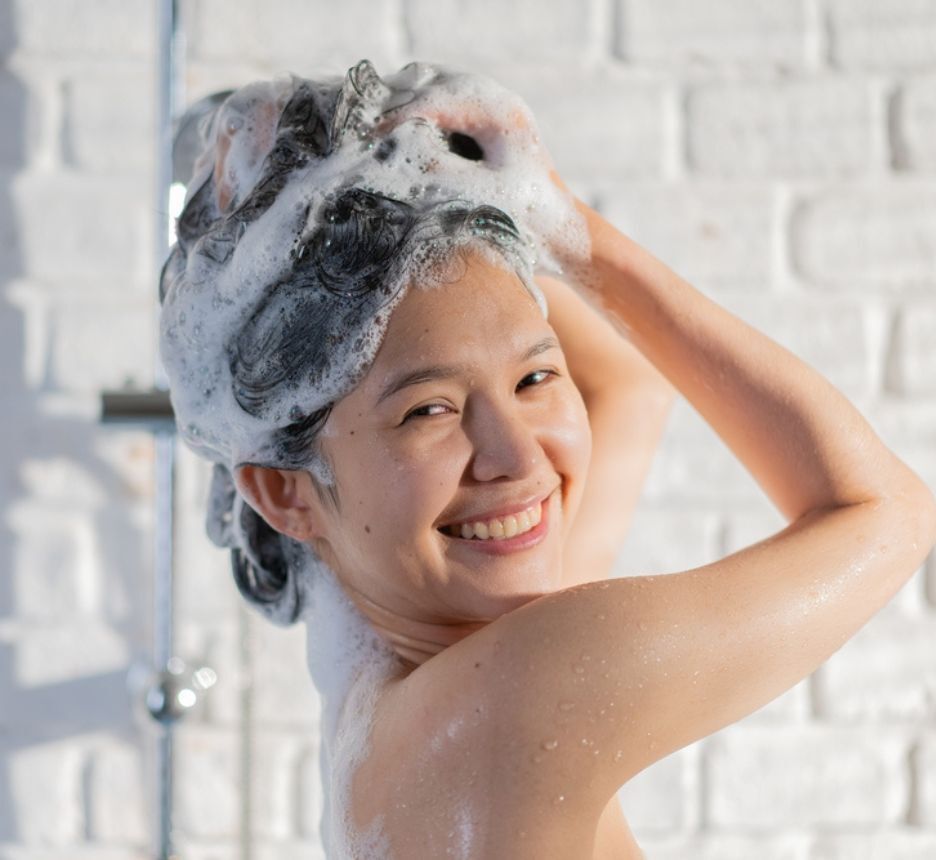 ngứa da đầu về đêm lựa chọn dầu gội có khả năng trị gàu cô gái đang cười tươi đang gội đầu dưới vòi hoa sen