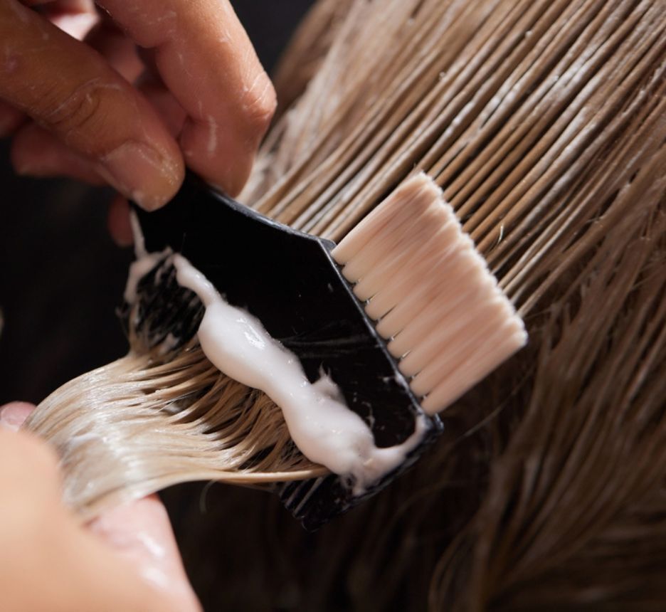 tẩy tóc là gì bàn tay đang cầm chổi chải thuốc tẩy lên tóc