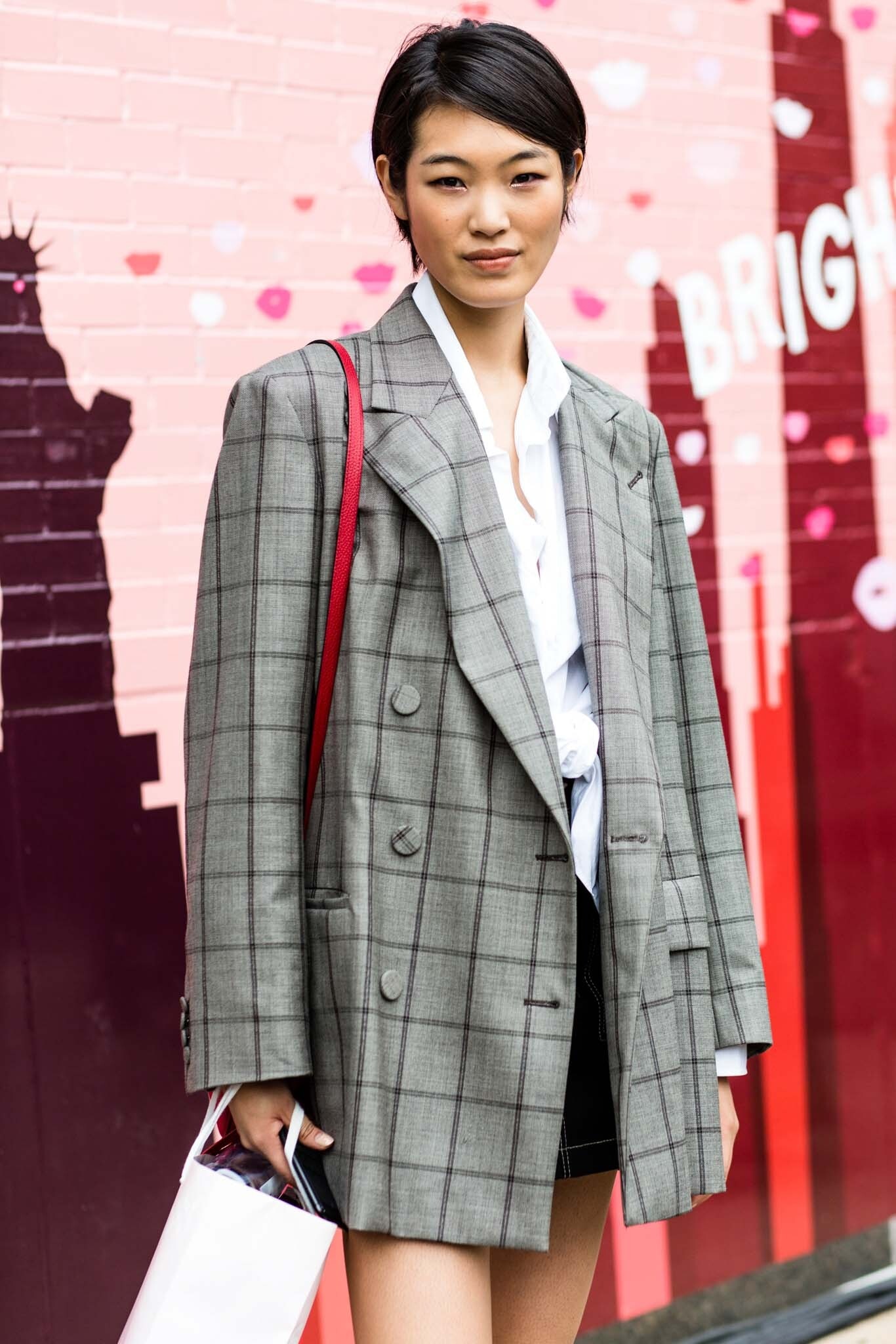 Woman with dark brown straight hair styled in a side swept pixie cut wearing a large grey blazer.