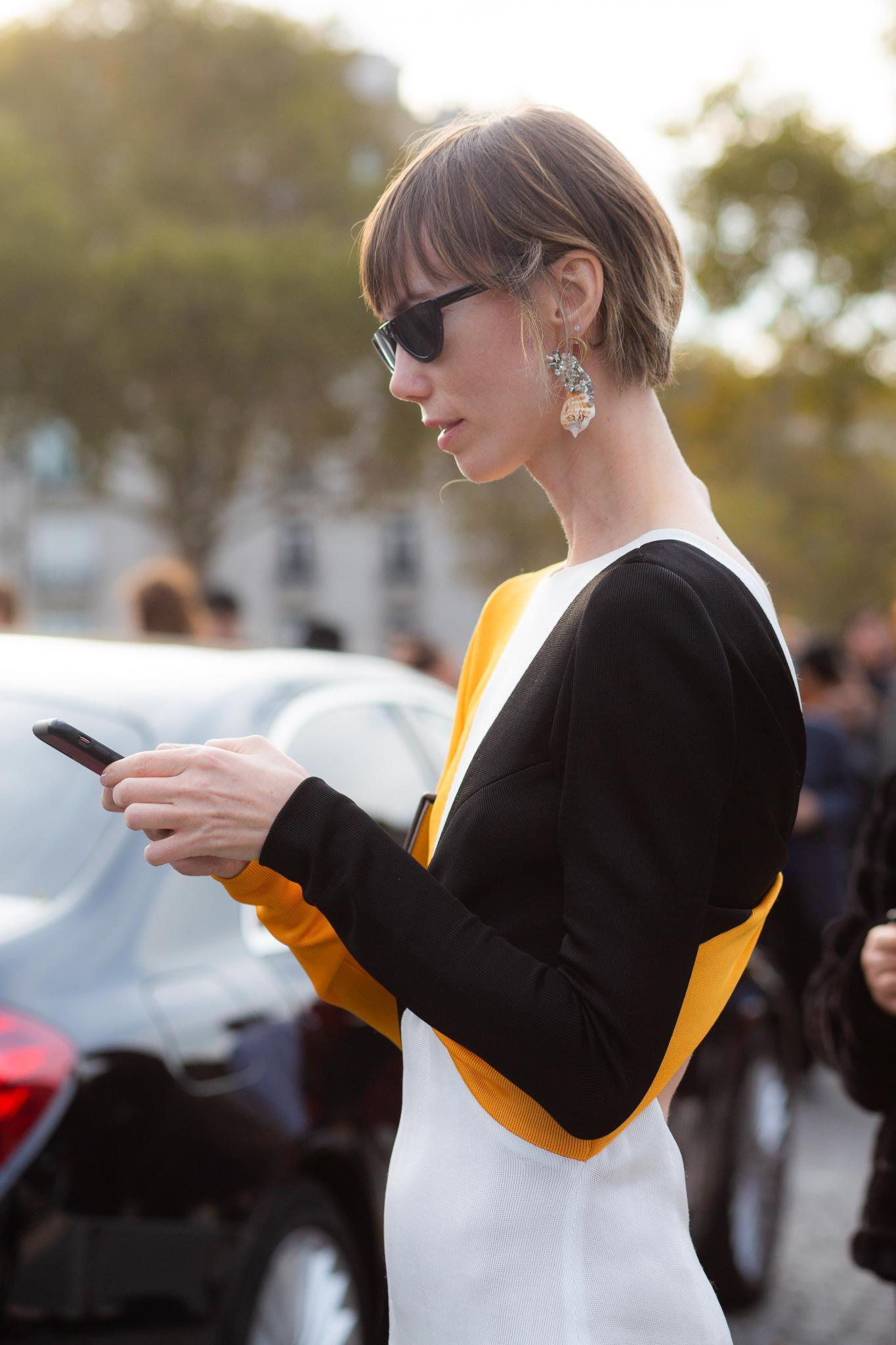 Short hairstyles for fine hair: Side profile of woman with fine straight light brown hair styled in a short bob looking at her phone.