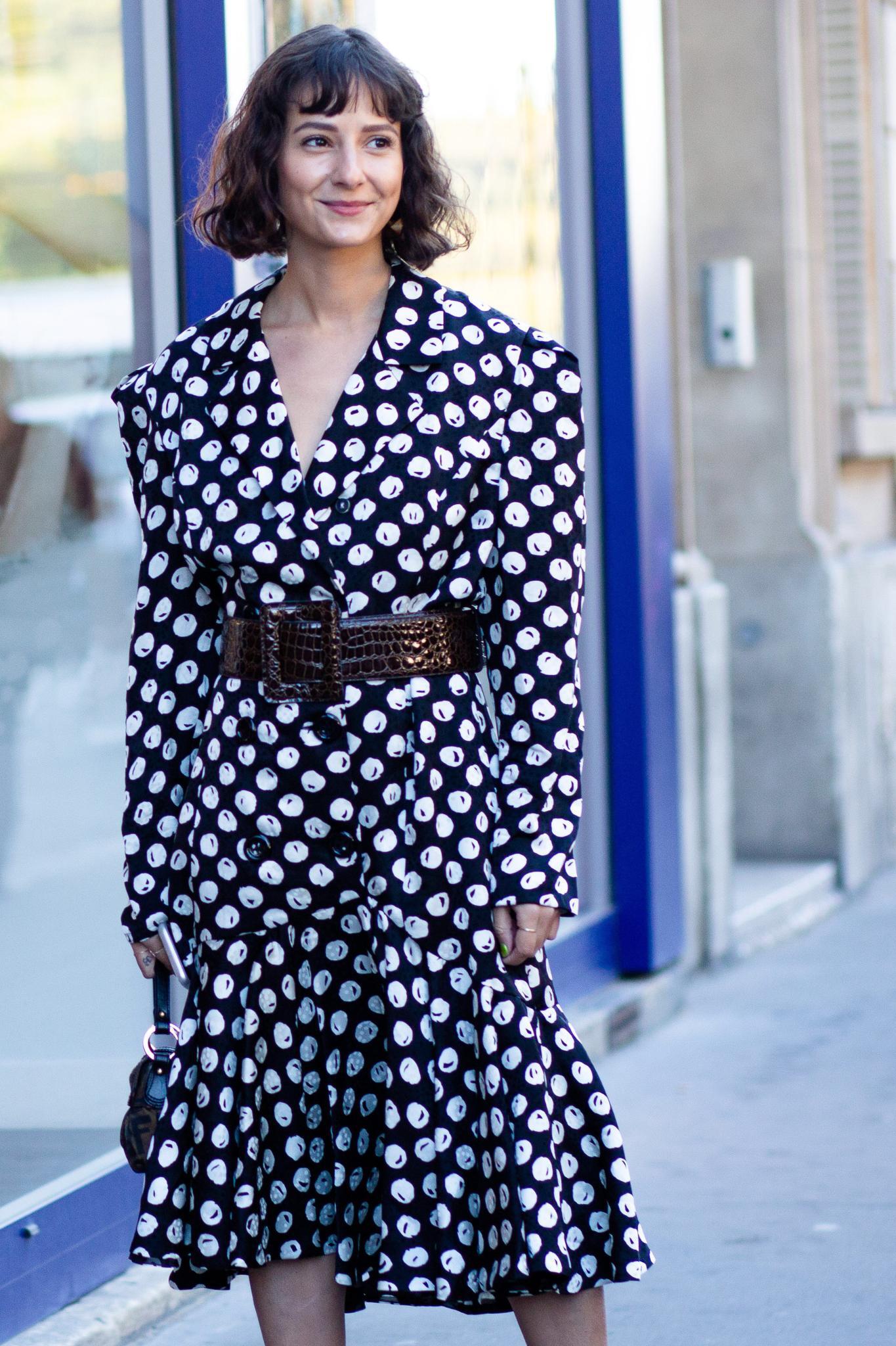 Woman with textured curly brown bob and bangs wearing a spotted dress.