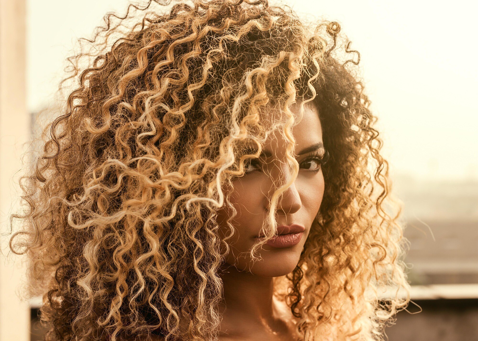 woman with big curly hair, brown base with blonde highlights