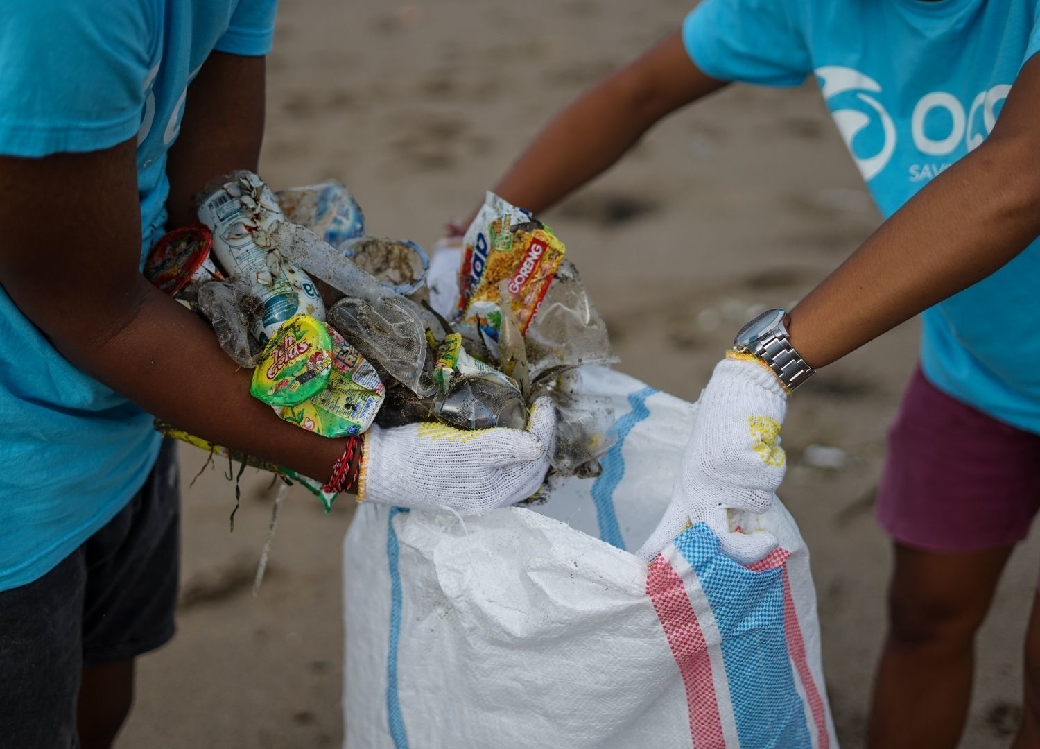 earth day: close-up image of two people on a beach clean-up, putting trash into a dirt bag