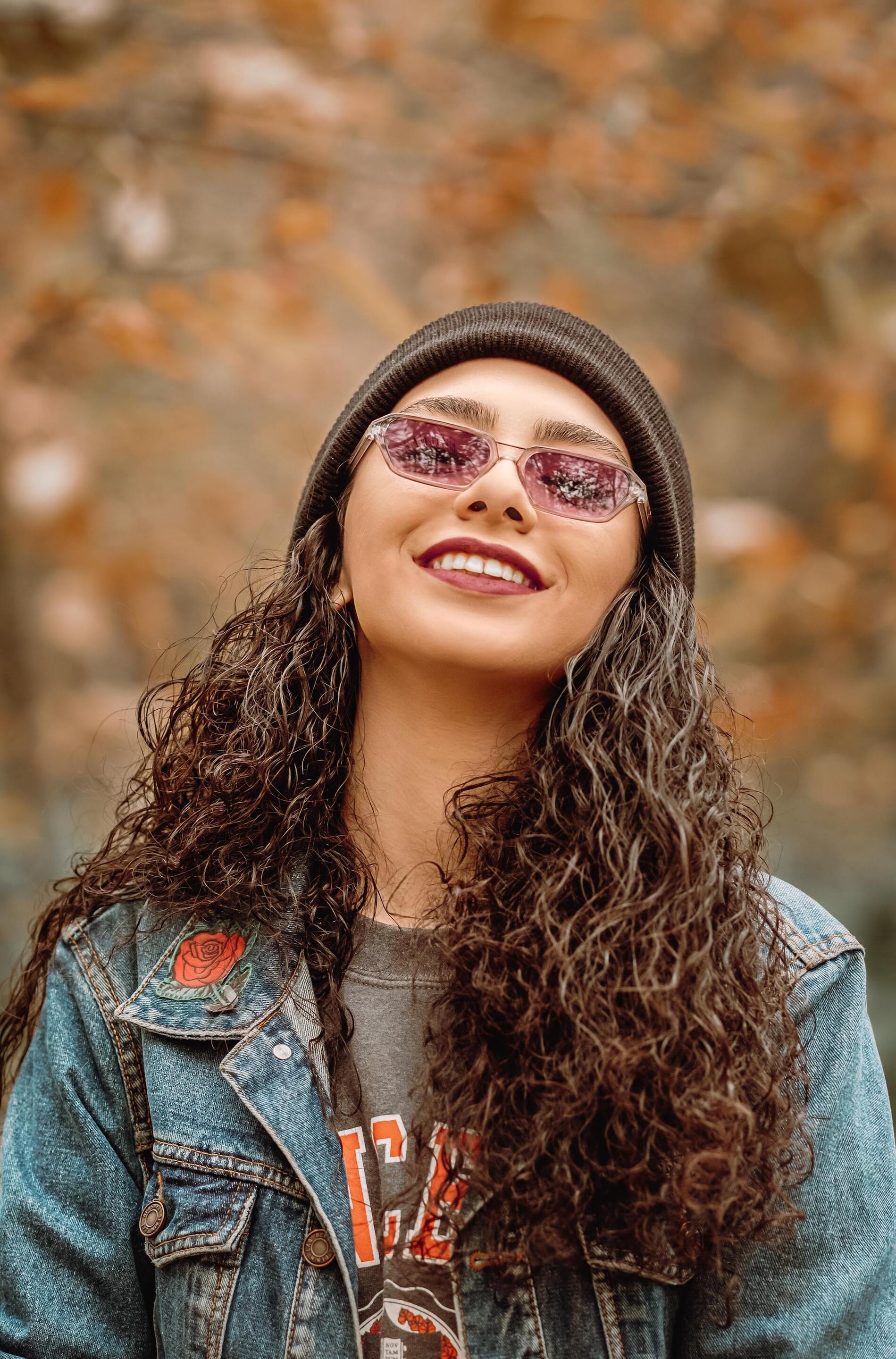 Woman with dark brown curl hair wearing a beanie and glasses