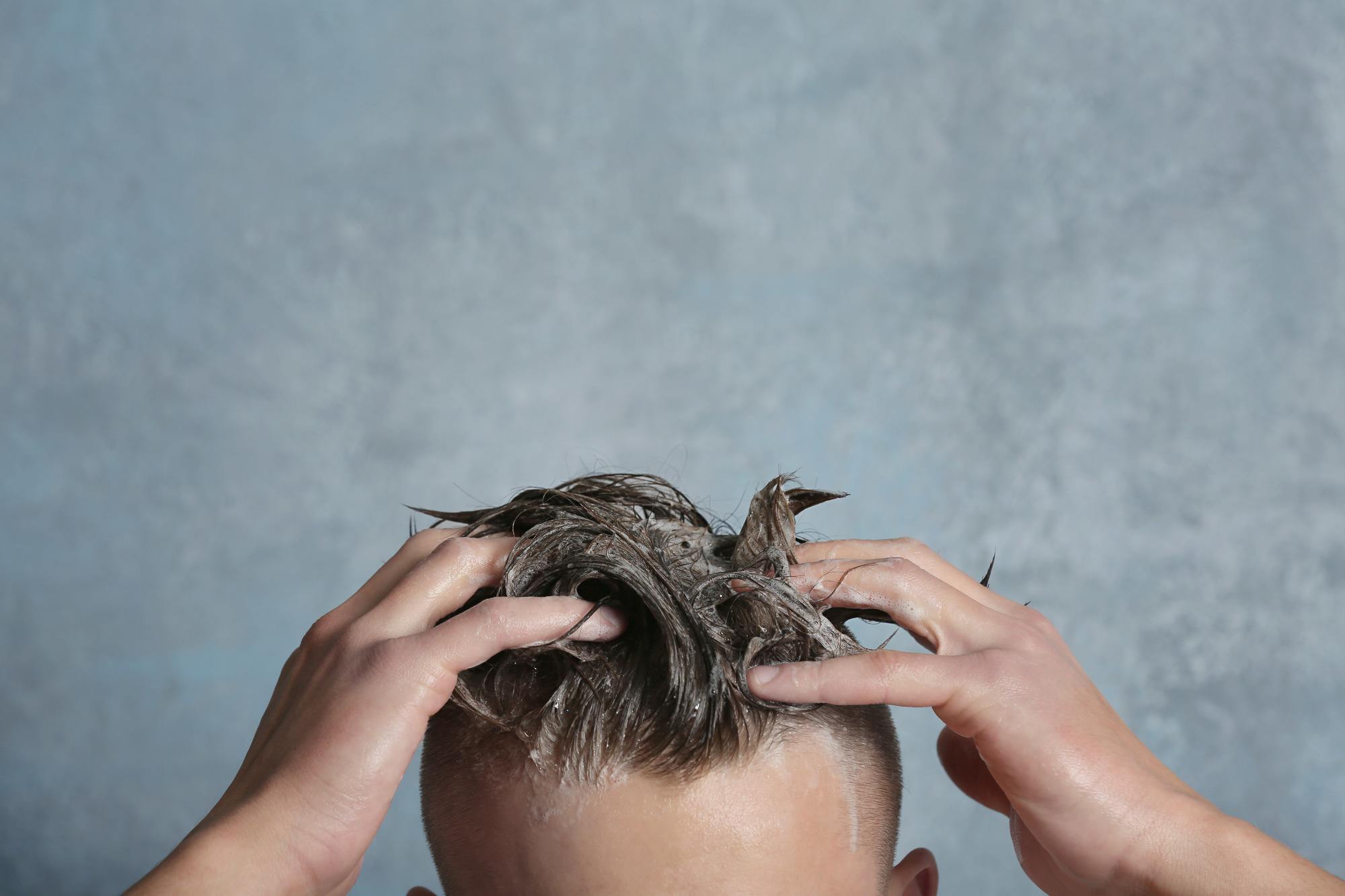 hair growth for men: Young man washing his hair on gray background