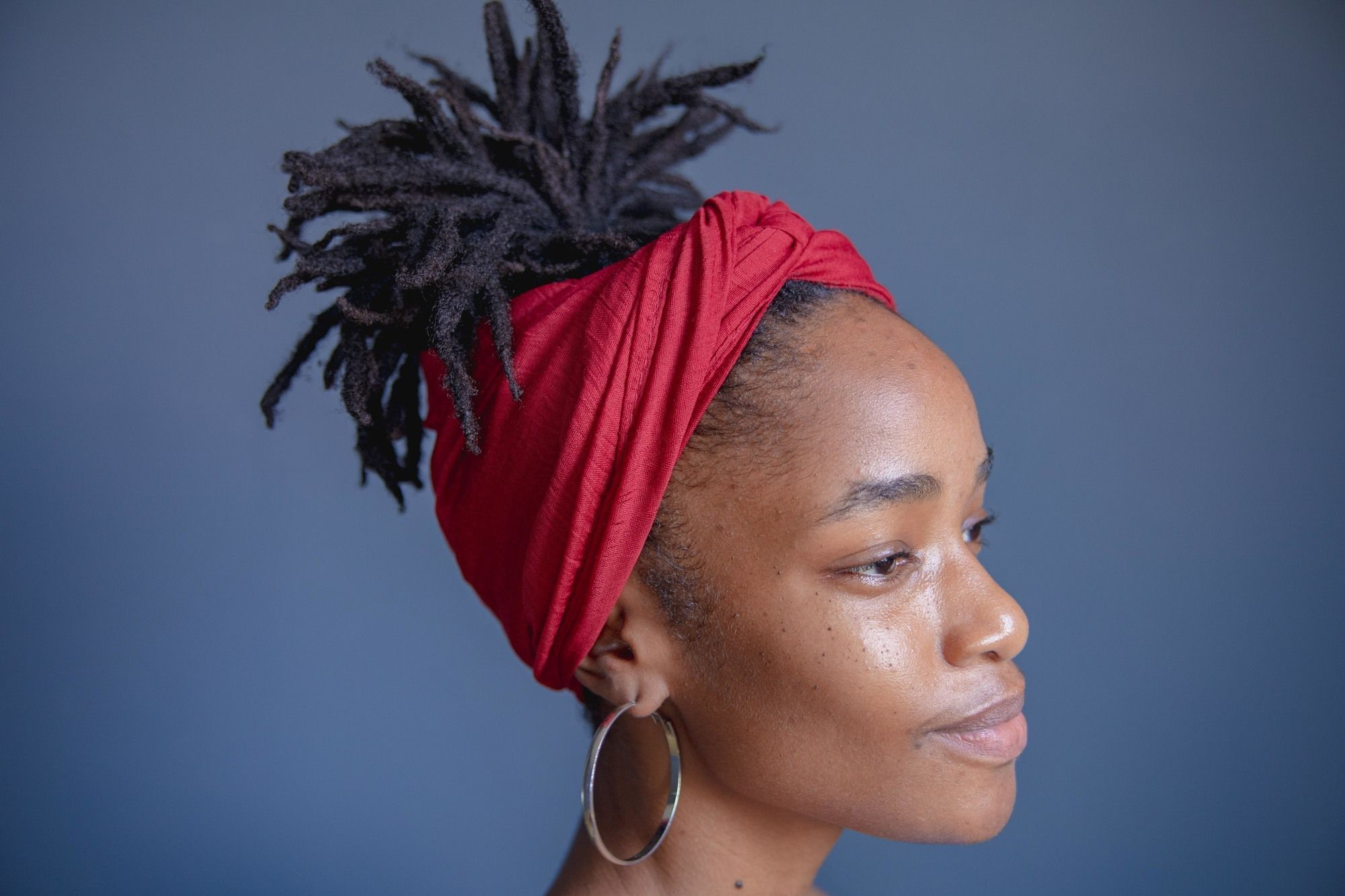 loadshedding hairstyles: woman with locs, tied up and wrapped with a bright red headband