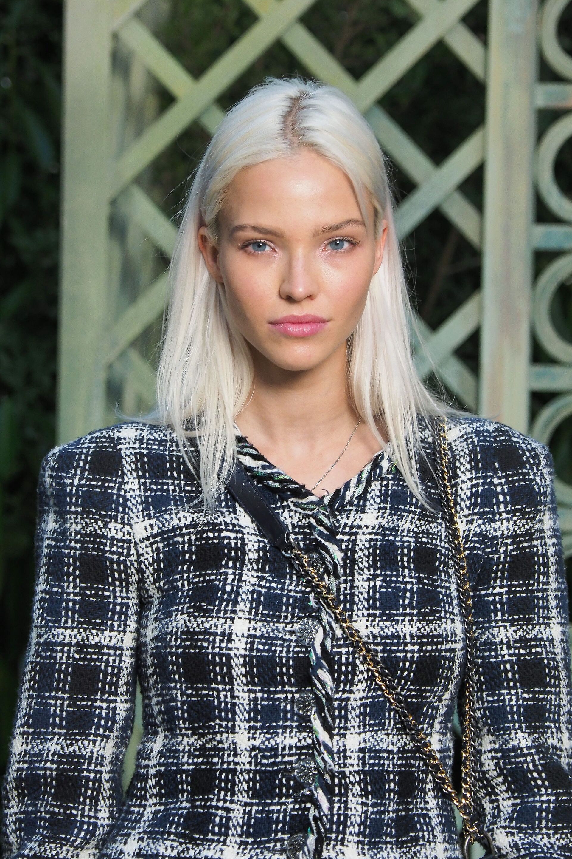 Sasha Luss with straight medium length platinum hair colour wearing a monochrome tartan jacket.