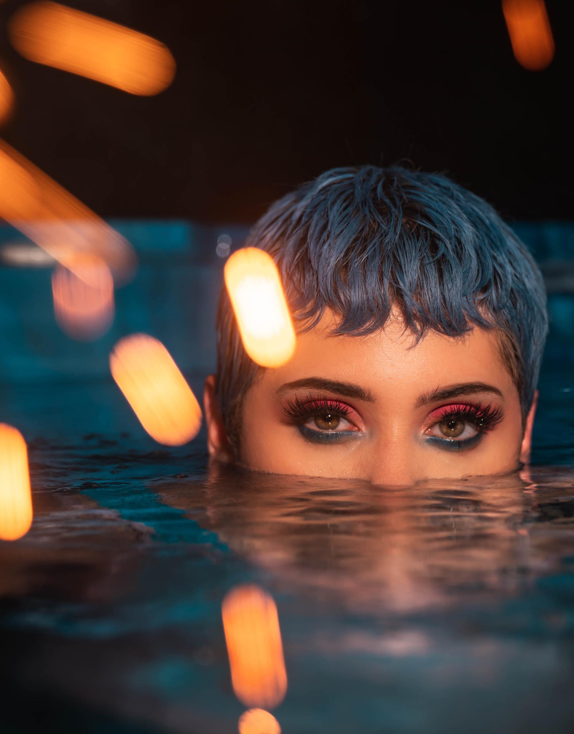 Cancer zodiac: woman in water with her hair and eyes showing; her hair is cut into a very short pixie cut with a cropped fringe and dyed blue