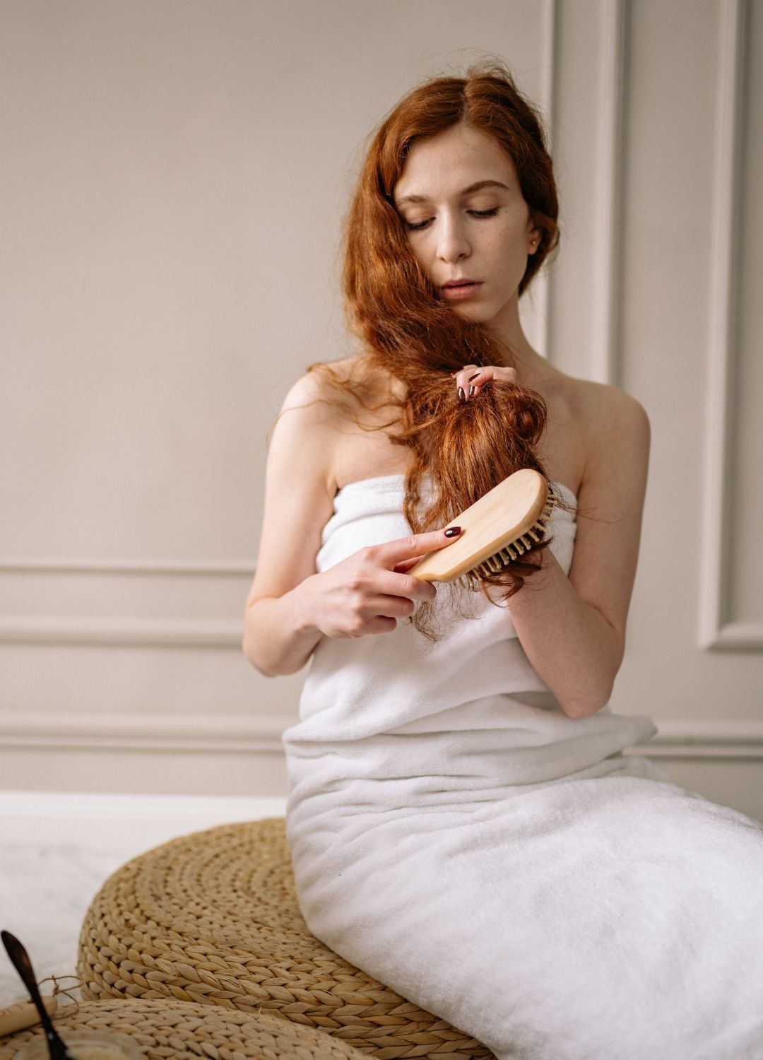 woman with long naturally red hair, brushing her hair with a wooden paddle brush