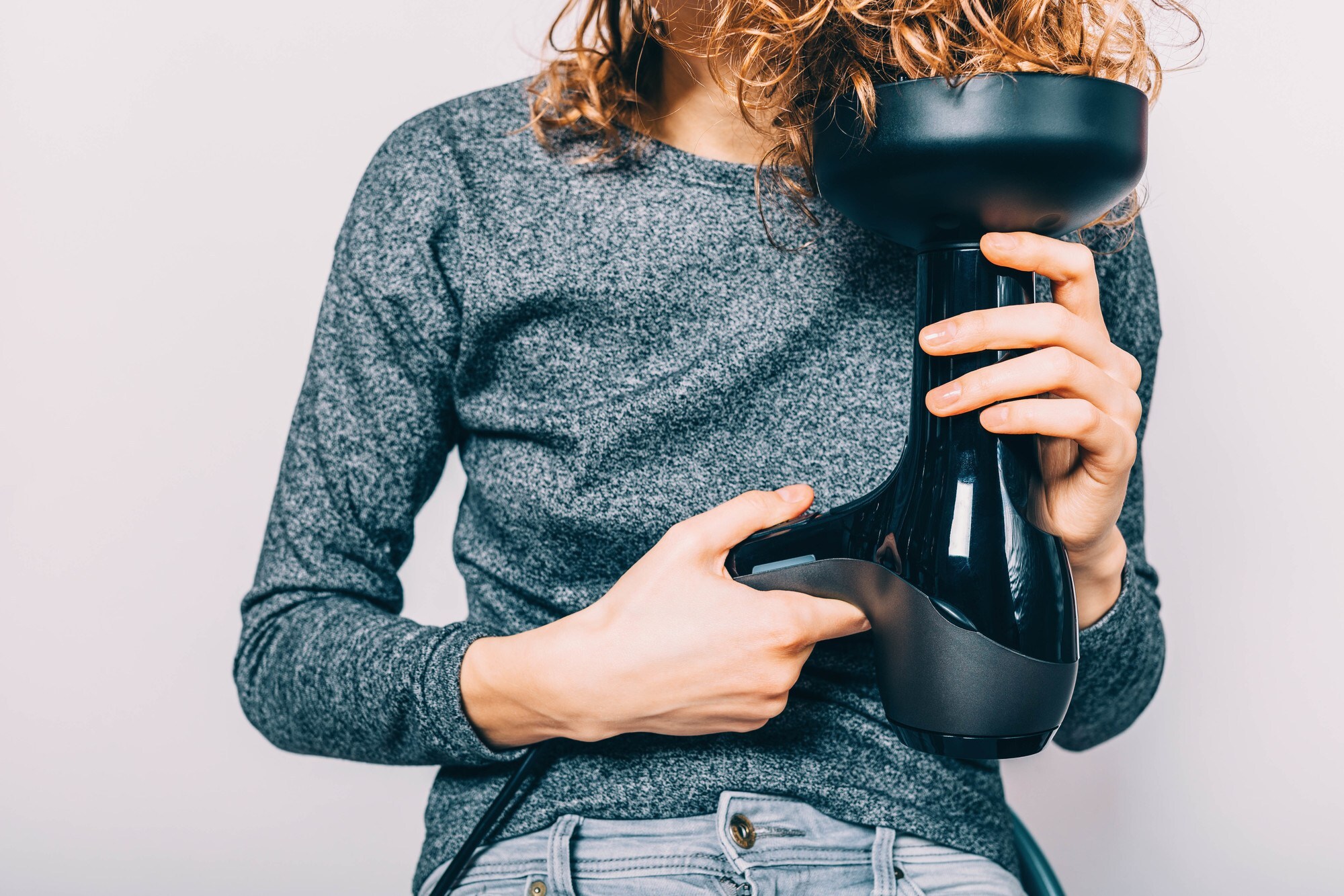 woman drying her curly hair with a hairdryer that has a diffuser attachment