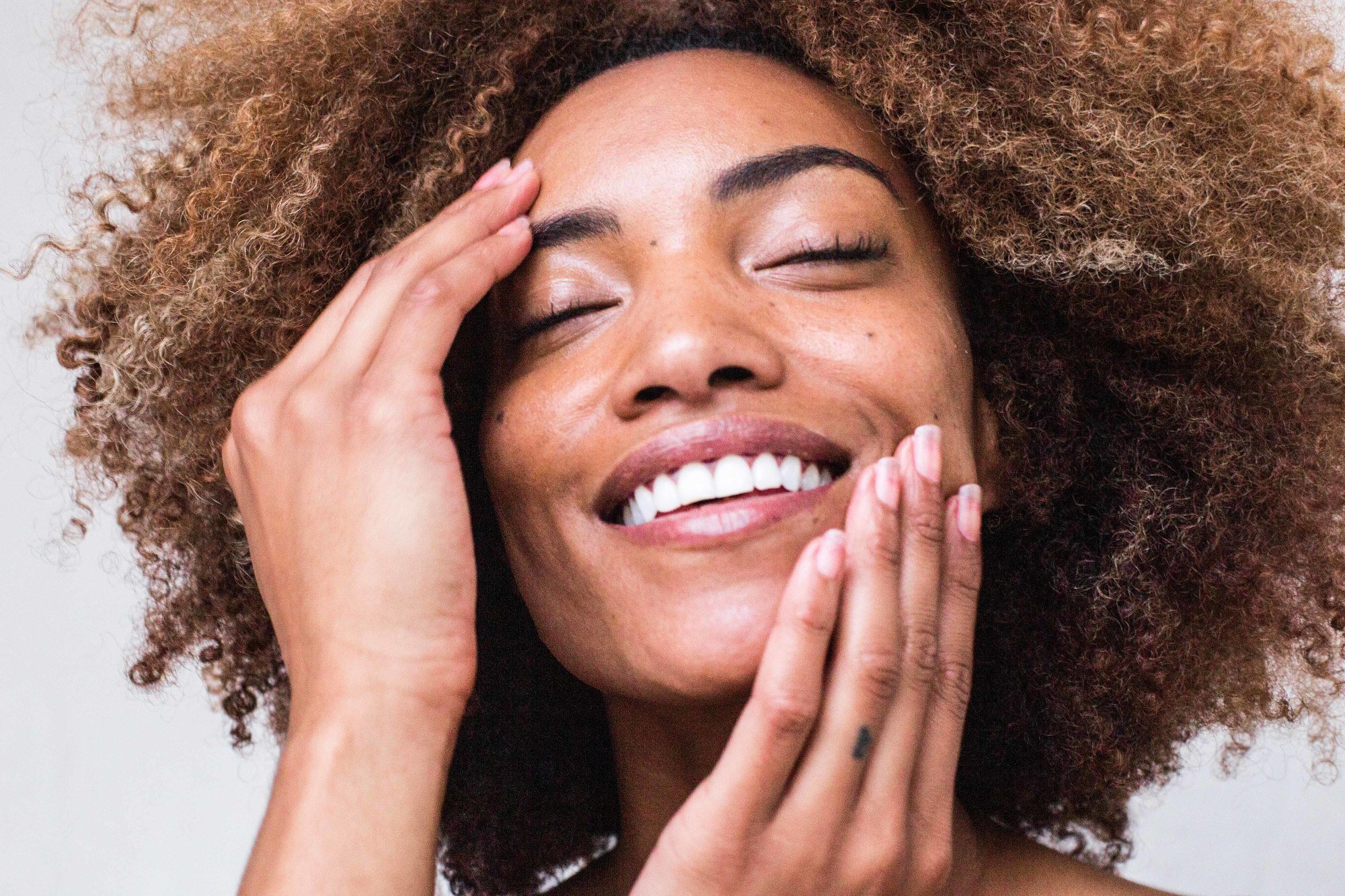 close up shot of a smiling woman with brownish blonde afro hair