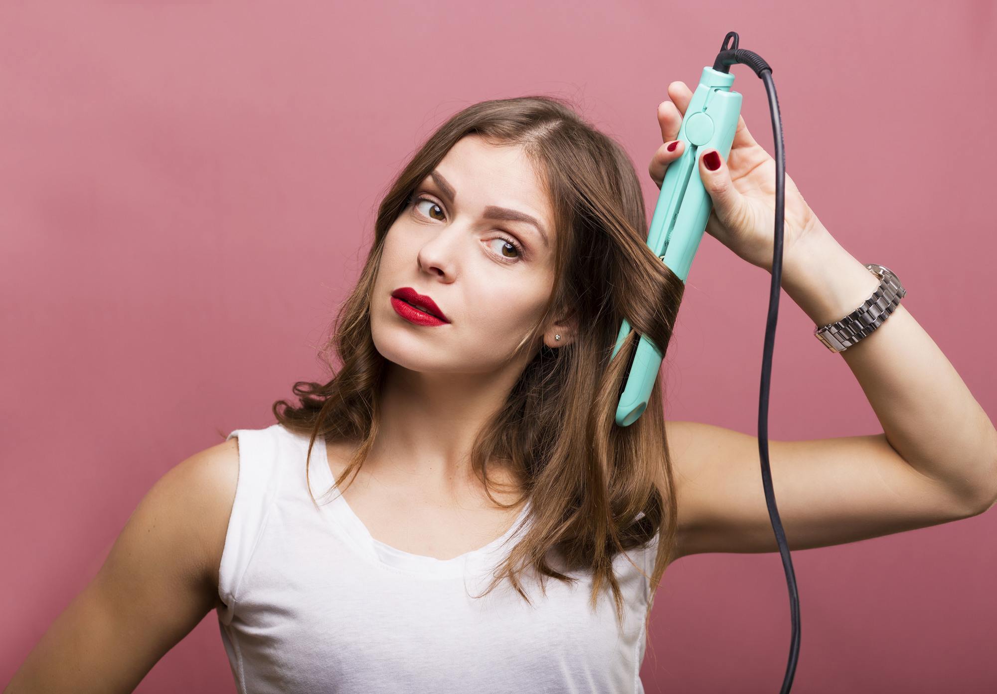 freshly dyed hair: woman heat styling her hair with a flat iron