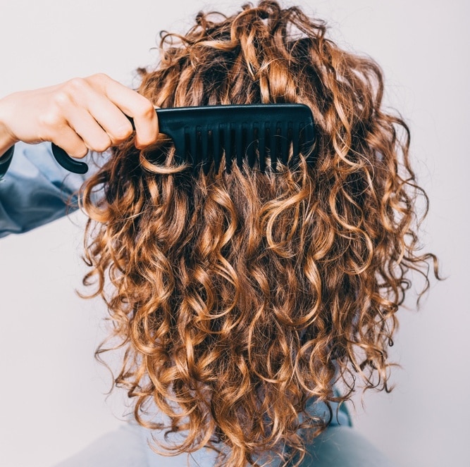 woman detangling natural hair with a wide toothed comb