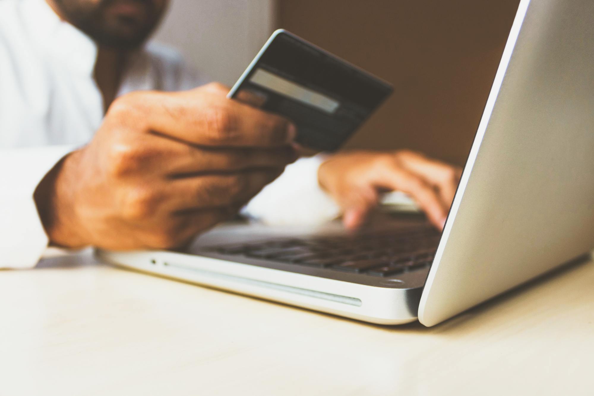 Black Friday tip: close-up shot of a person seated in front of a laptop, holding their bank card