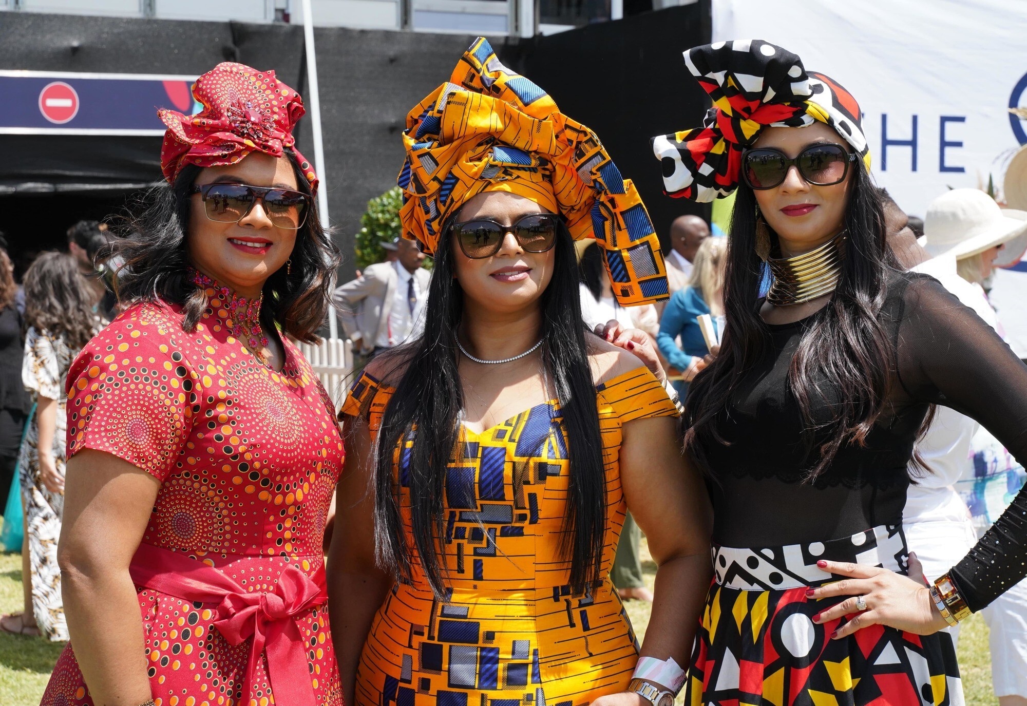 three women at the sun met 2020 with brightly big, coloured head wraps and sleek black hair