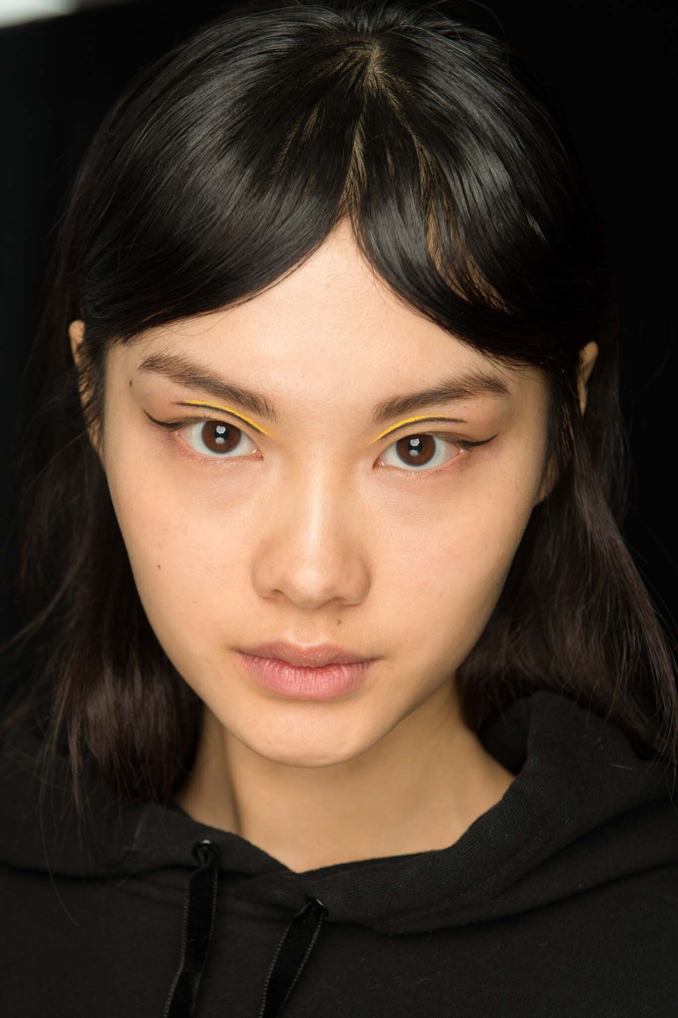 New hairstyle: Model with dark brown hair and centre parted bangs wearing a black top.