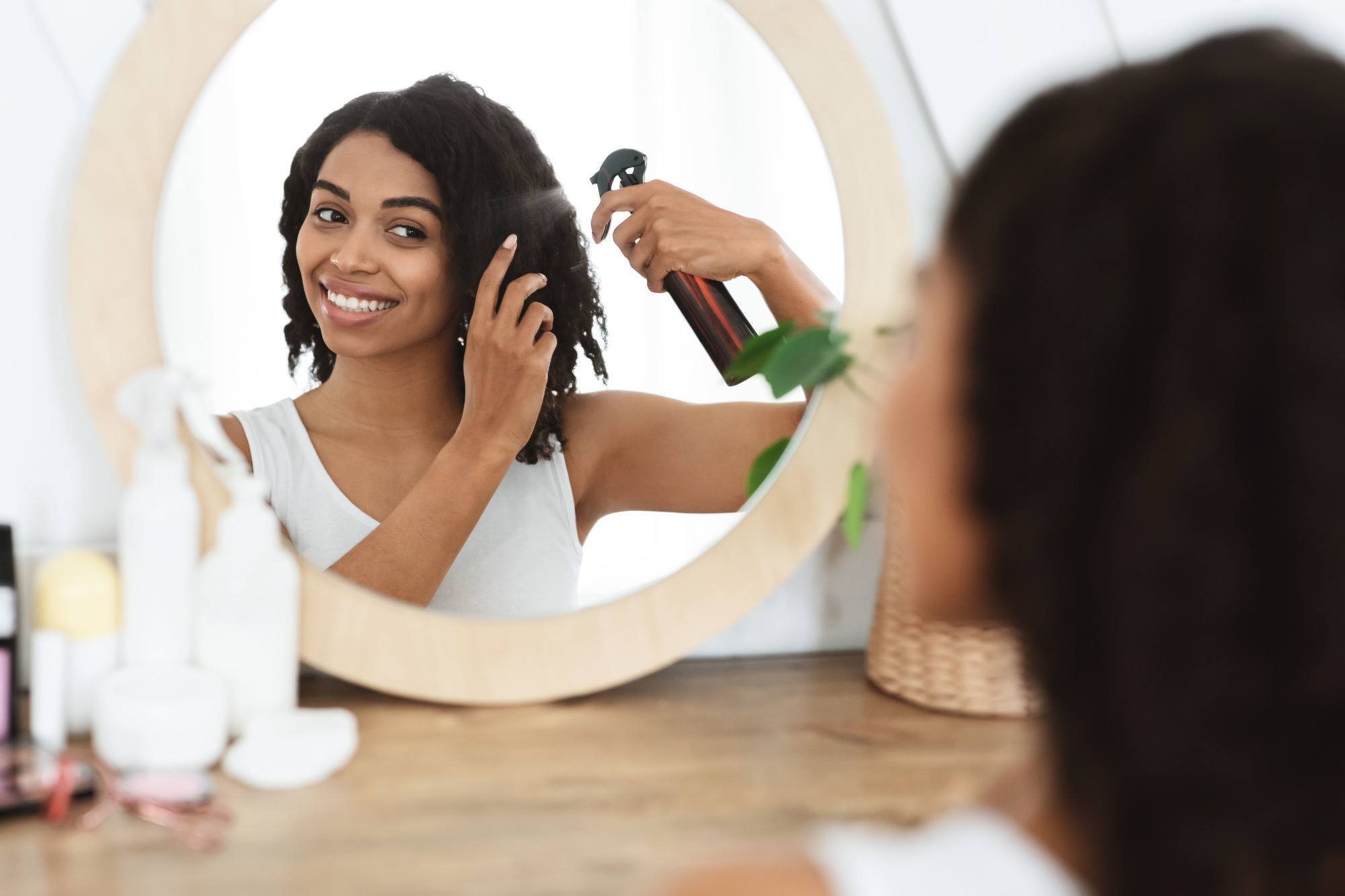 hair hacks for thick hair: woman spraying product on her naturally curly hair