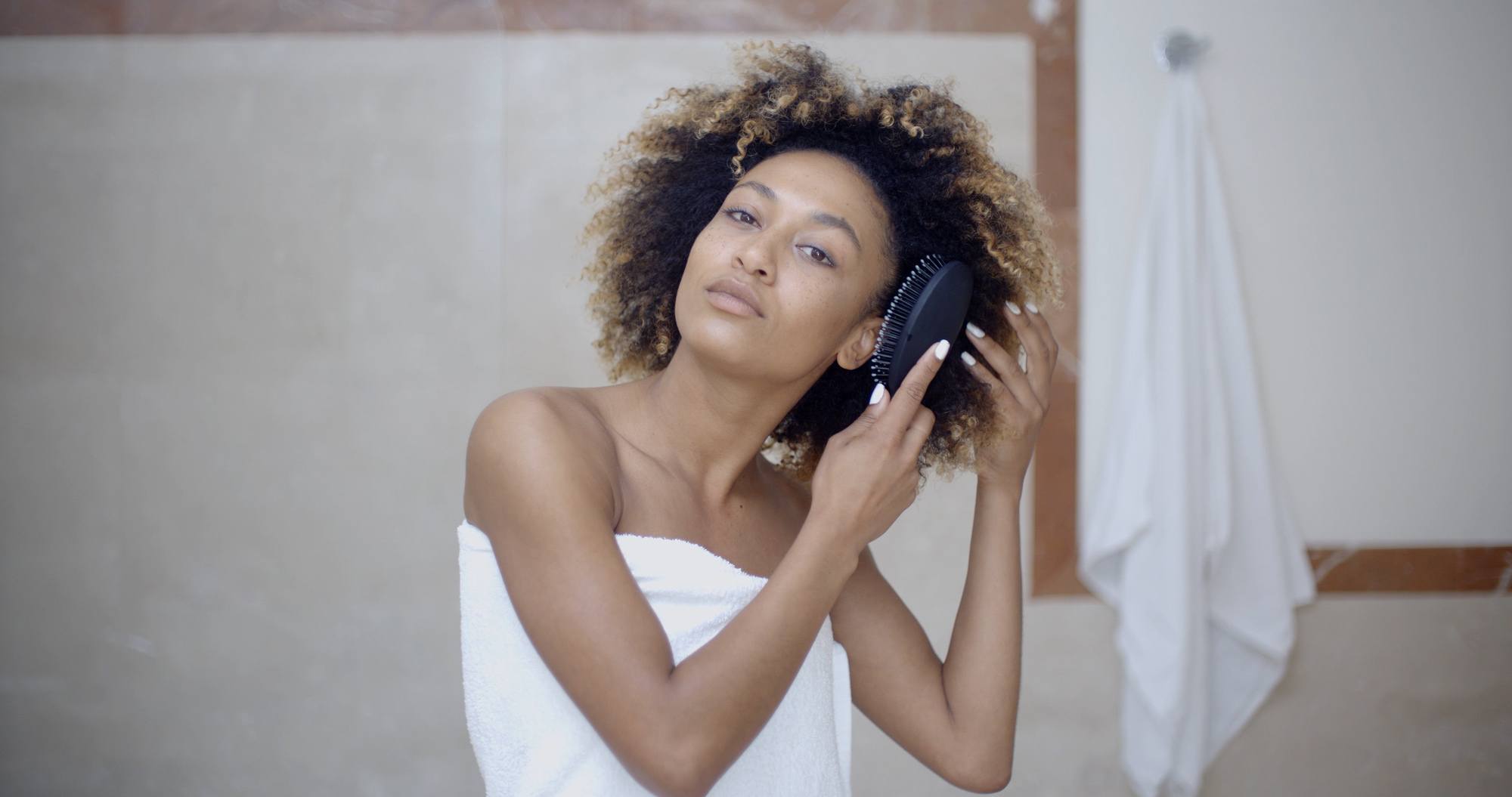 hair hacks for thick hair: woman brushing out her naturally curly hair