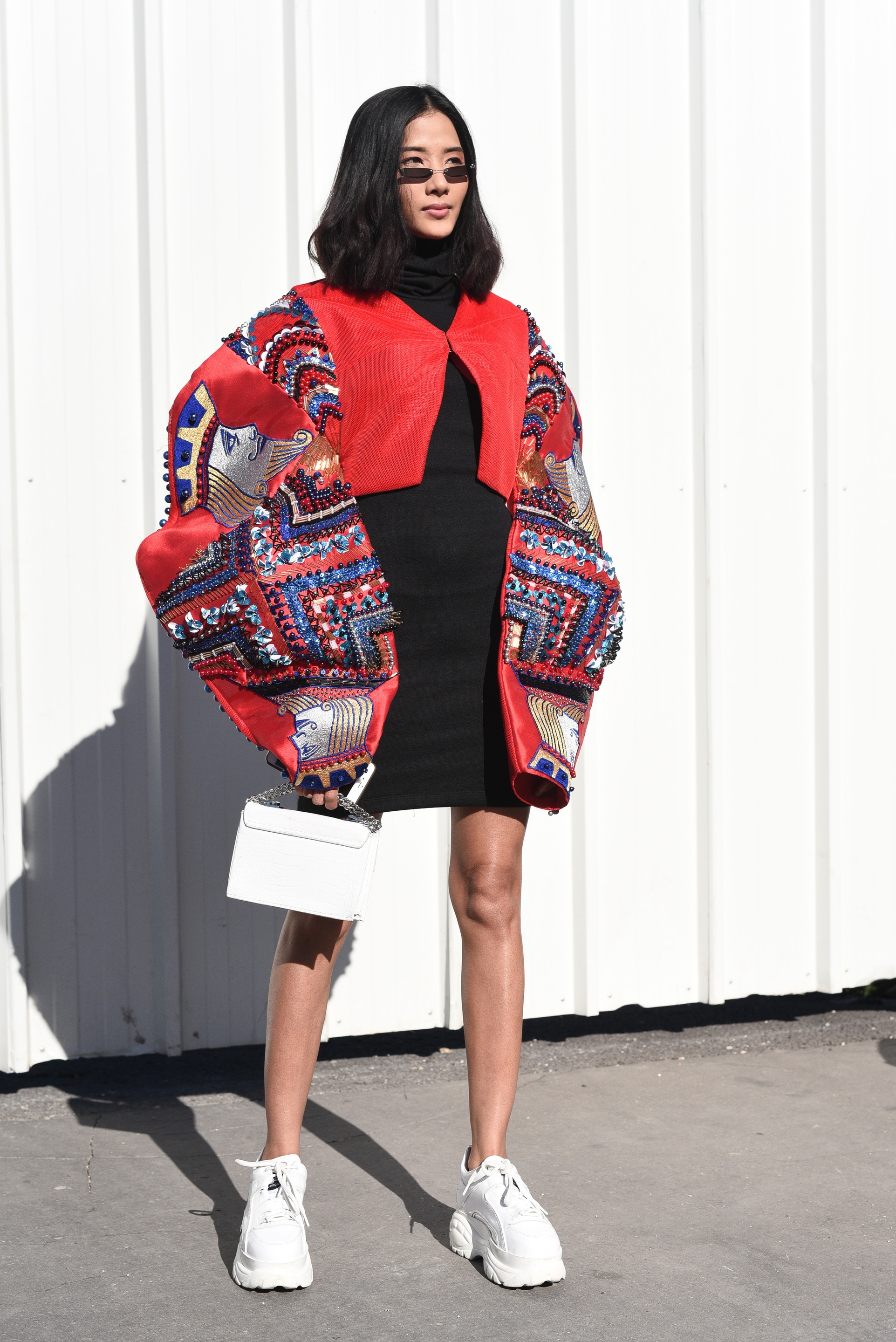 Hairstyles for thick hair: Woman with dark brown long bob with soft waves in street style image. Woman is wearing micro sunglasses and puffer oversized dress.