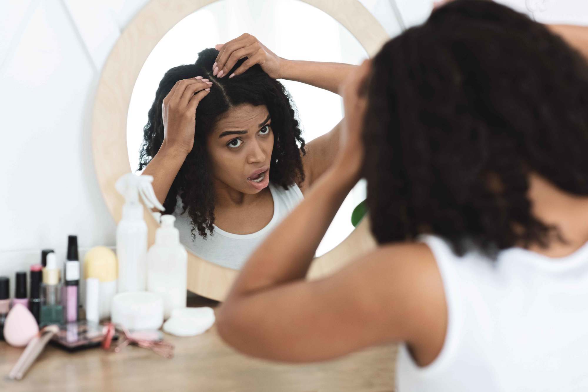 woman with natural curly hair looking at her dry scalp