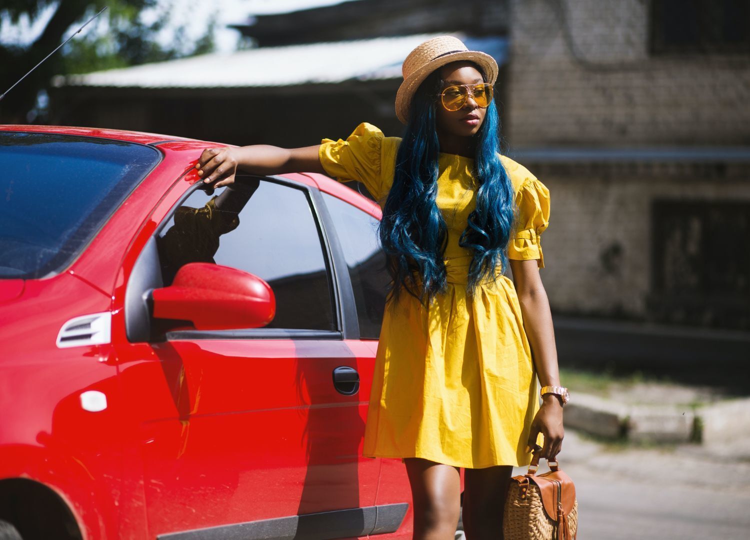 woman standing next to a bright red car; the woman has long wavy royal blue hair