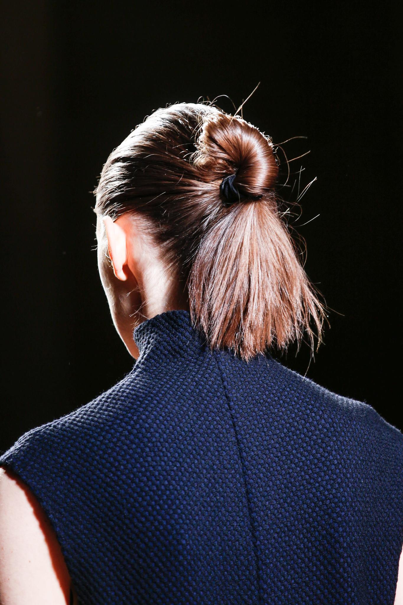 Hairstyles for long hair: Back view of woman on Victoria Beckham FW15 runway with long brown hair styled in a twisted bun with ends hanging loose. Woman is wearing a sleeveless navy high neck top.