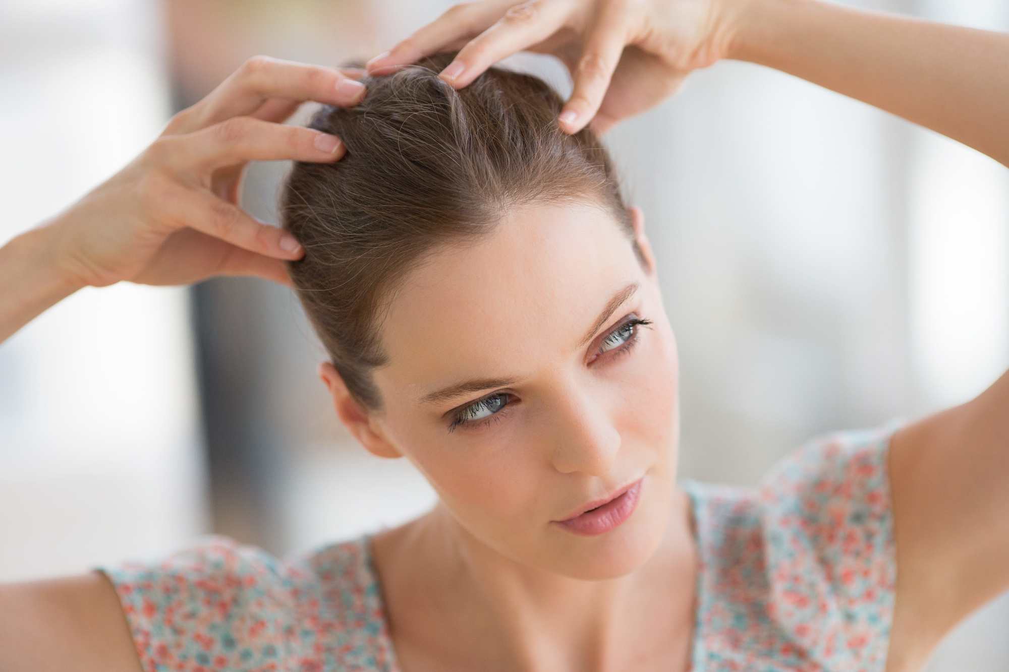 Itchy scalp: Woman with brown hair in a updo with her fingers touching her scalp