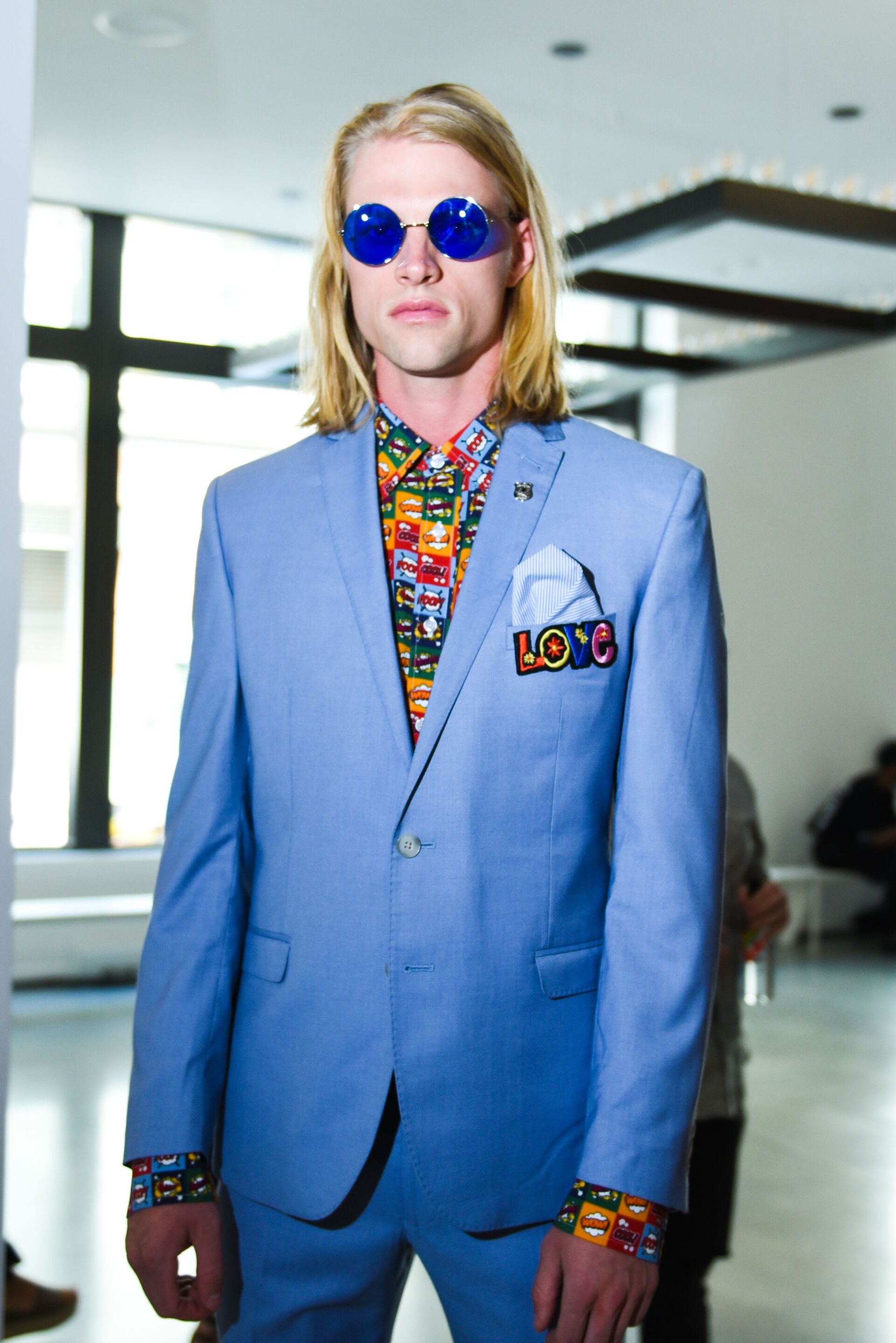 Men's hairstyles: Model with shoulder length blonde straight hair men's fashion week presentation wearing a blue suit and sunglasses
