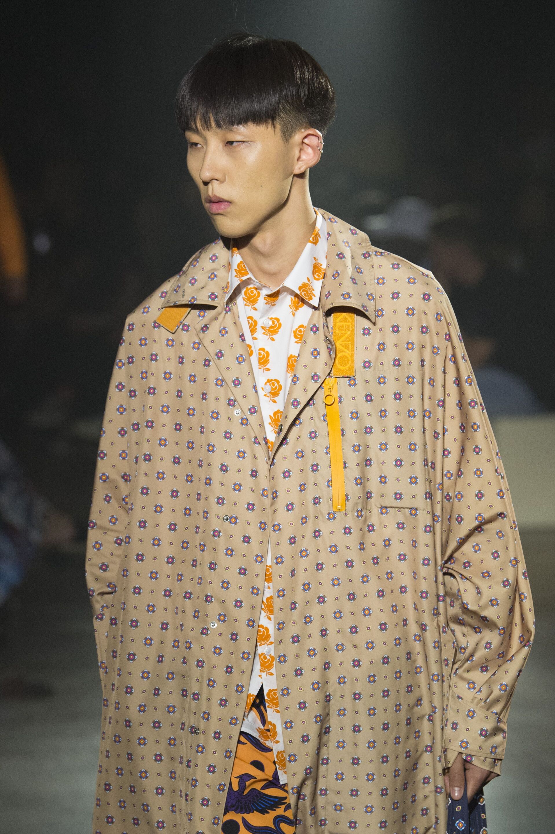 Men's hairstyles: Man on runway with straight dark brown mushroom cut hair wearing beige overcoat.