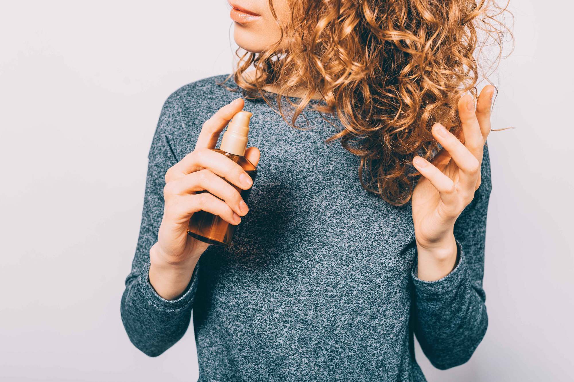 woman with curly auburn hair applying oil onto hair
