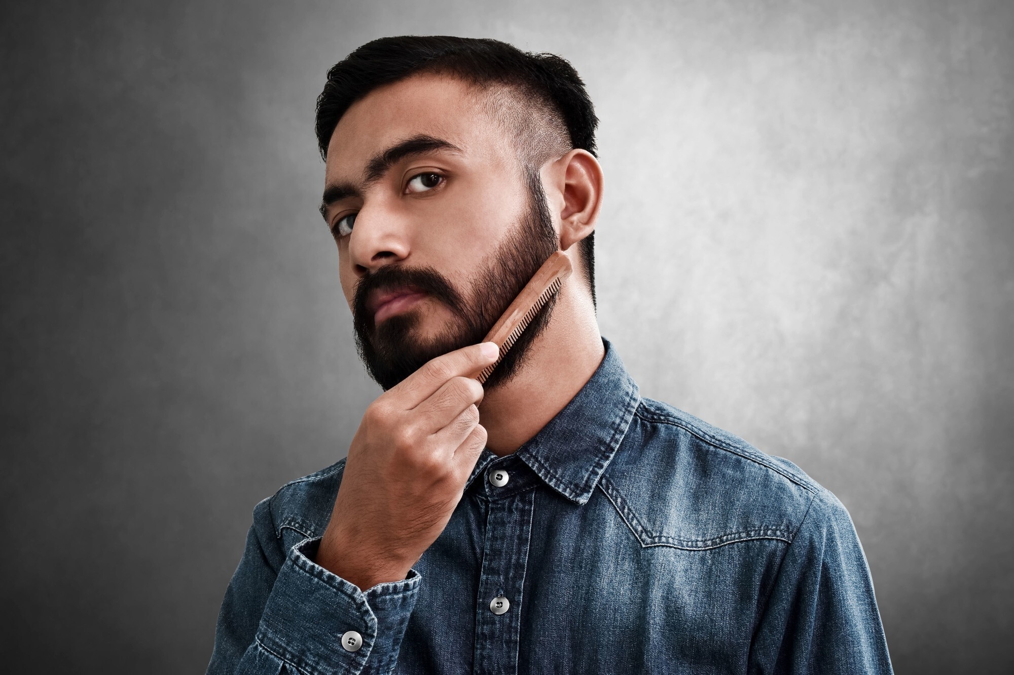 beard care: man combing a wooden comb through neatly trimmed hair