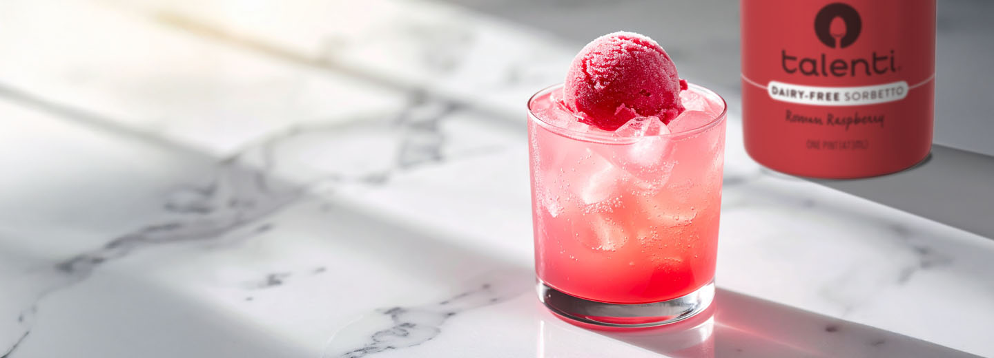 A pink Roman punch in a glass with a scoop of sorbetto on top with a jar of Talenti Roman Raspberry Sorbetto in the background