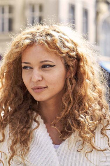 Mulher loira de cabelo cacheado ilustra a matéria sobre cortes para quem tem muito cabelo
