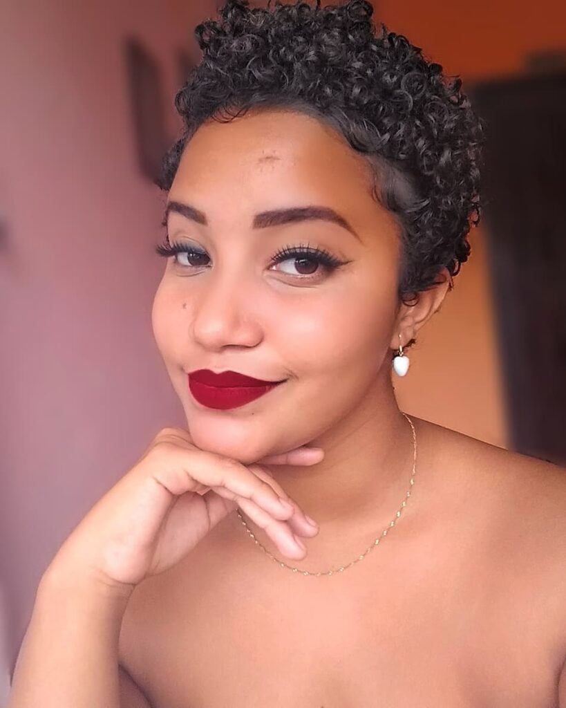 Mulher de batom vermelho posa com a mão no queixo e cabelo curto cacheado 3c estilo joãozinho