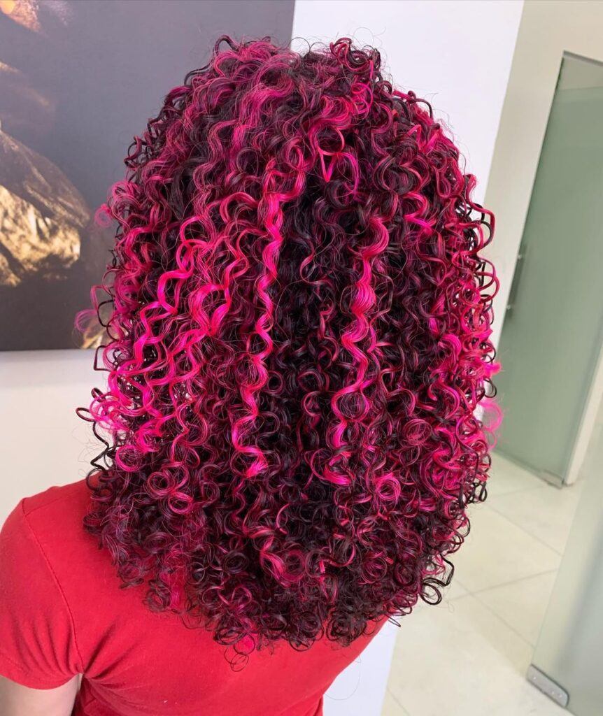 mulher de costas com blusa vermelha e mechas rosas no cabelo cacheado longo