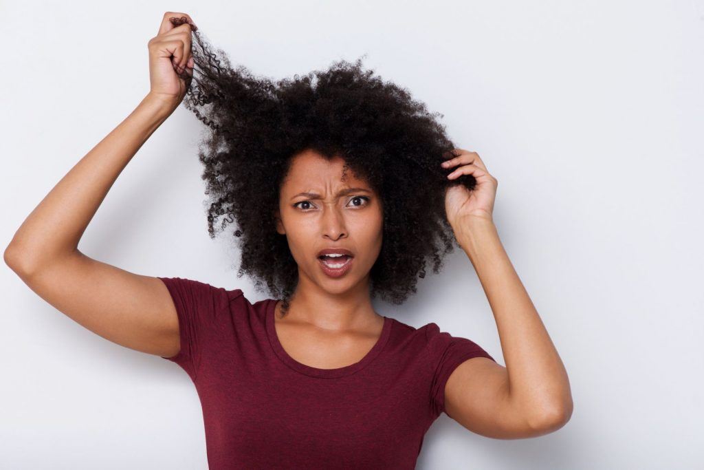 Mulher de cabelo crespo preocupada com fios danificados na parte da frente