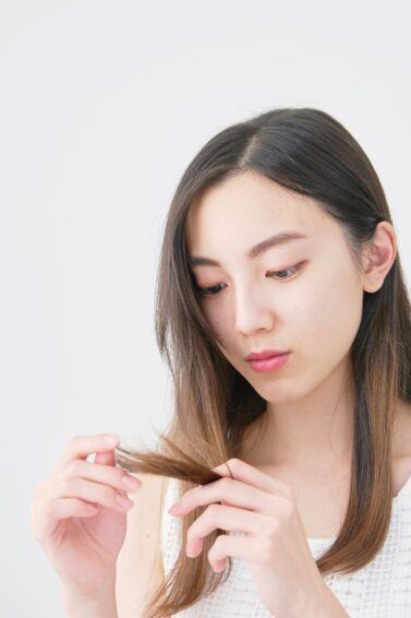 mulher olhando preocupada para as pontas do cabelo quebradas